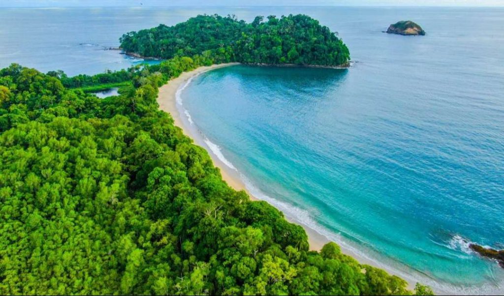 Scenic view of Manuel Antonio National Park in Costa Rica with lush rainforest, white sand beach, and turquoise ocean waters.